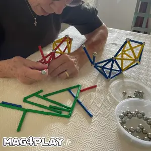 Un résident senior concentré et souriant, assemblant patiemment une structure complexe avec des barrettes et des sphères Geomag lors d’un atelier cognitif Mag4play à Lyon, dans le Rhône, en Rhône-Alpes et en Suisse romande.