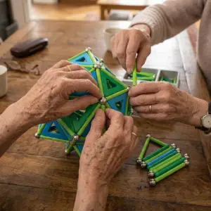 Gros plan sur les mains d'un senior manipulant des barrettes Geomag pendant un atelier cognitif Mag4Play à Lyon