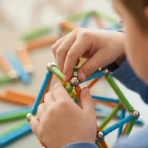 Gros plan sur les mains d'un enfant assemblant des barrettes et des sphères Geomag pendant un atelier Mag4Play dans le Rhône.