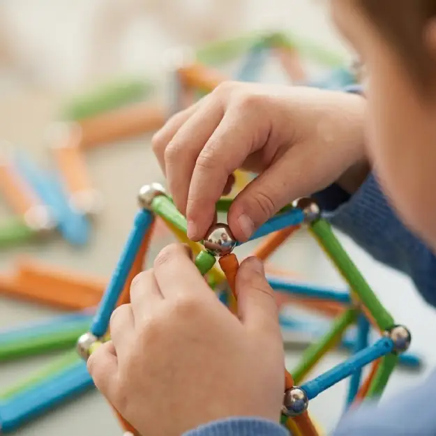 Gros plan sur les mains d'un enfant assemblant des barrettes et des sphères Geomag pendant un atelier Mag4Play dans le Rhône.